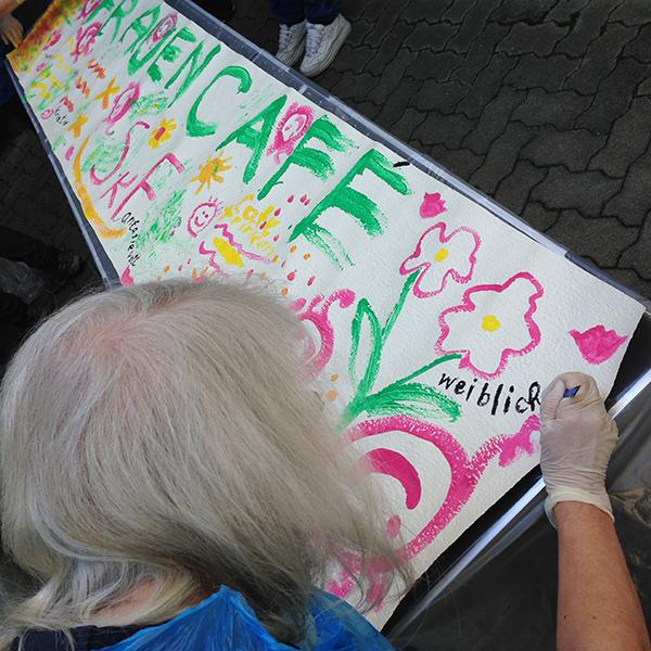 Frau beim Malen eines "Frauencafé"-Plakates